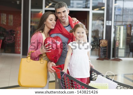 Father and mother push young daughter in shopping trolley through mall