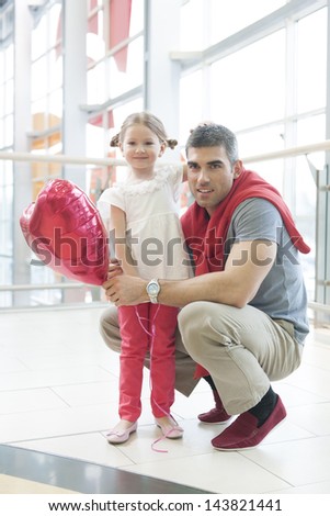 Father kneels with younger daughter holding balloon