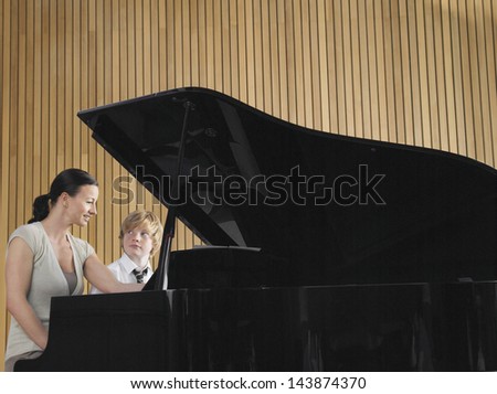 Happy teacher with boy playing piano in music class