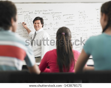 Teacher teaching on whiteboard to high school students in classroom