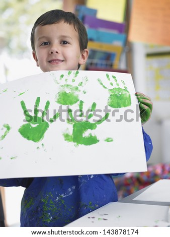 Portrait of young boy presenting his finger painting in art class
