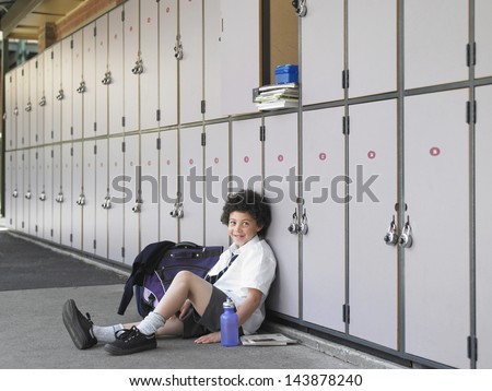 Portrait of happy boy sitting on floor against school lockers