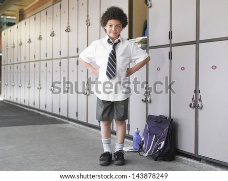 Portrait of happy boy with hands on hips standing by school lockers