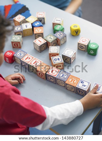 Cropped little boy playing with alphabet blocks in classroom