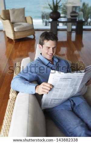 Happy young man reading newspaper on sofa at home