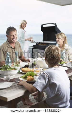 Family of four enjoying barbecue against the sea