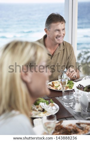Happy middle aged man enjoying food with woman in foreground against the sea