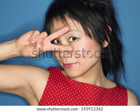 Closeup portrait of a Chinese woman looking through fingers against blue background