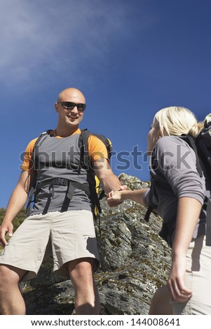 Man helping woman climb onto boulder against the blue sky