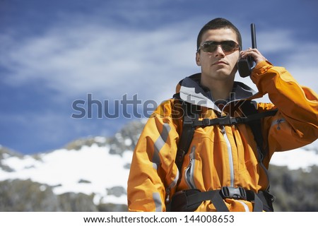 Smart young man using walkie talkie against blurred snow capped mountain
