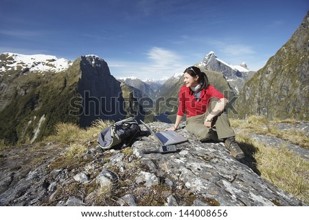 Young woman sitting with laptop on boulder against mountains