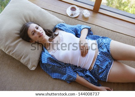 Portrait of a young woman in pajamas lying on couch with coffee on window sill