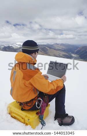 Rear view of a male hiker using laptop on snowy mountain landscape