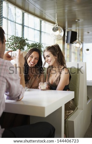Man photographing happy female friends in the cafe