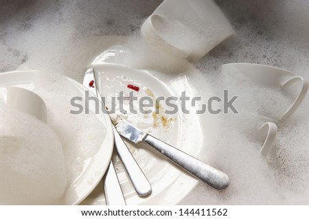 Closeup of a stack of dirty dishes and silverware in sink with bubbles