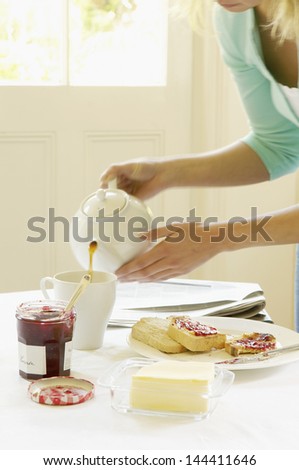 Closeup of hands pouring tea into cup on dining table at home