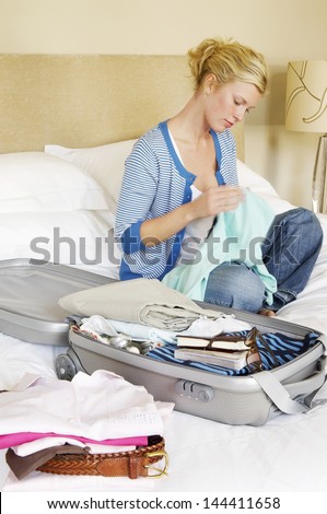 Woman sitting cross legged on bed next to folded clothes and packed suitcase