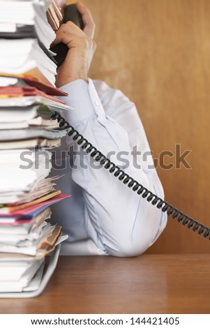 Cropped shot of a man talking on telephone behind a stack of paperwork at desk