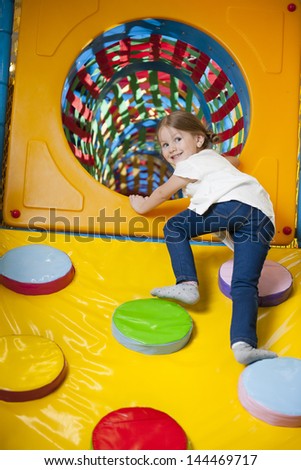 Young girl climbing up ramp into tunnel at soft play center