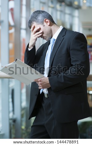 Business man reads document and covers face