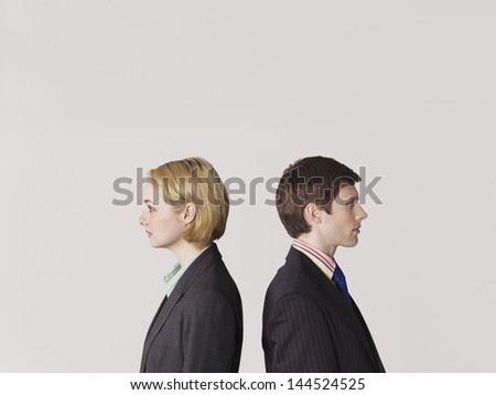 Side view of two business people standing back to back on gray background