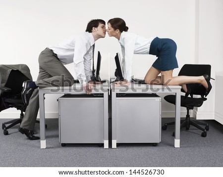 Side view of a business couple kissing over desks in the office