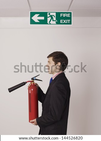 Side view of a young businessman holding fire extinguisher under exit sign