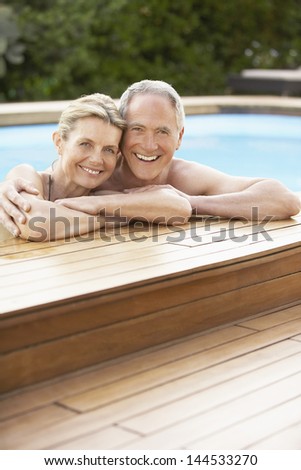 Portrait of happy middle aged couple relaxing on the edge of swimming pool