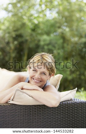 Portrait of happy middle aged woman relaxing on sofa in garden