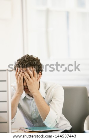 Stressed young male executive sitting in cubicle with head in hands