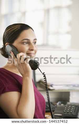 Portrait of young Asian businesswoman using landline phone at desk