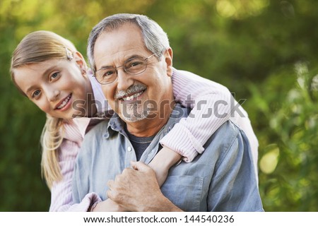 Portrait of young girl embracing grandfather from behind in backyard