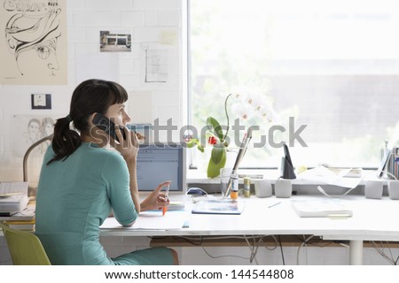 Young female artist using cell phone at desk Young female artist using cell phone at desk