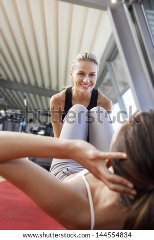 Happy female coach assisting woman in doing sit-ups at gym