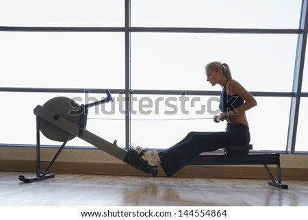 Side view of fit young women using rowing machine in health club