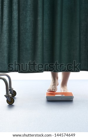 Person stepping onto weighing scales behind curtain in hospital