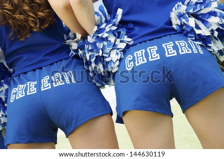 Closeup rear view midsection of two cheerleaders holding pom poms