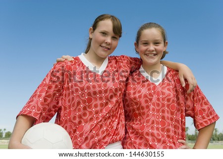 Portrait of happy two young girls dressed to play football against clear sky