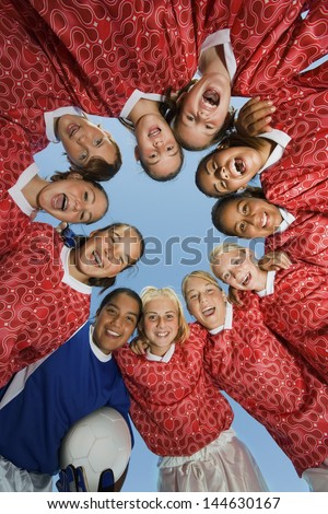 Portrait of girls\' soccer team forming a huddle against clear blue sky