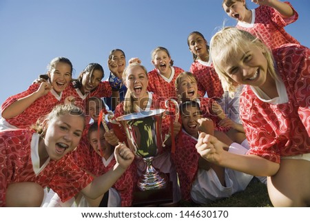 Portrait of excited girls\' soccer team holding trophy against clear sky