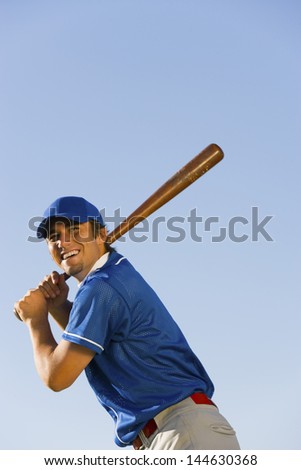 Low angle view of a happy baseball player swinging baseball bat against clear blue sky