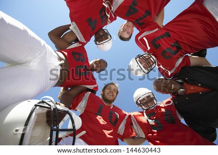 Low angle view of rugby players with coach forming huddle against clear sky