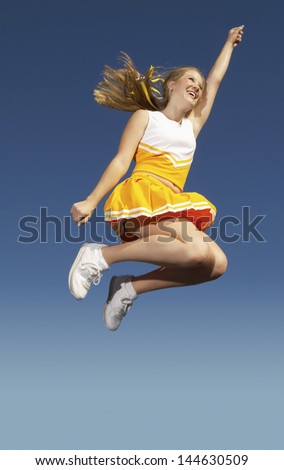 Low angle view of a cheerleader in yellow costume jumping midair against clear sky
