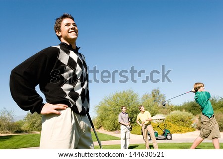 Three male golfers watching other golfer teeing off