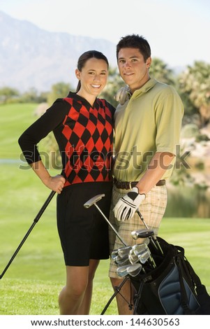 Portrait of a smiling golf couple standing together with golf bag on course