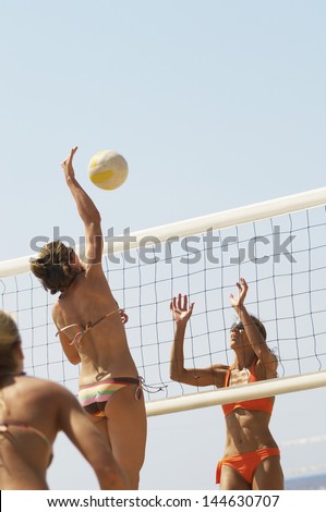 Player jumping to spike volleyball over net as opponent defends on beach