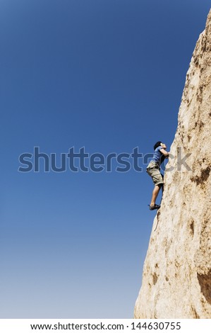 Side view of a young man free climbing on cliff against clear blue sky
