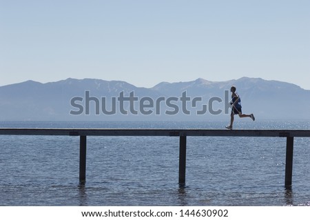 Side view of a man running along pier over sea with mountains in the background