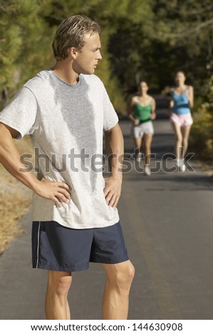 Male jogger pausing for breath on path with female friends in background