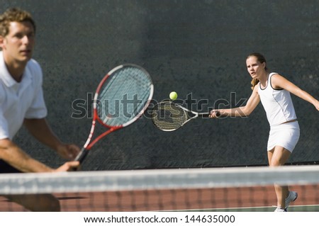 Mixed doubles player hitting tennis ball with partner standing near net